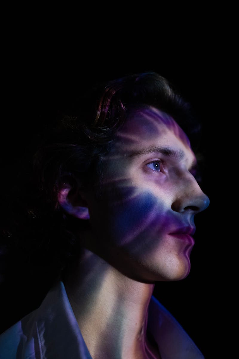 Dramatic portrait of a young man with colorful light refraction on his face in a dark setting.